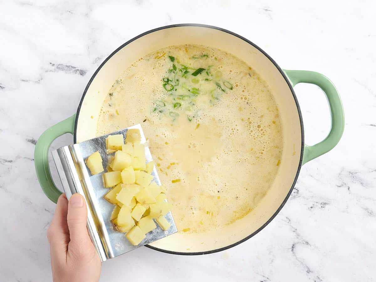 Diced potatoes and green onions added to a pot of potato leek soup.