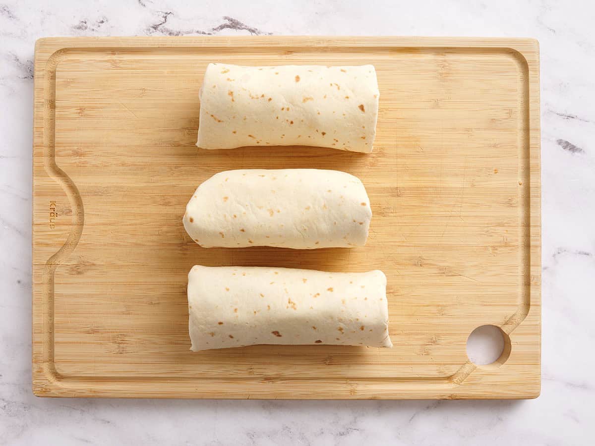 Three rolled tuna wraps on a wooden cutting board.