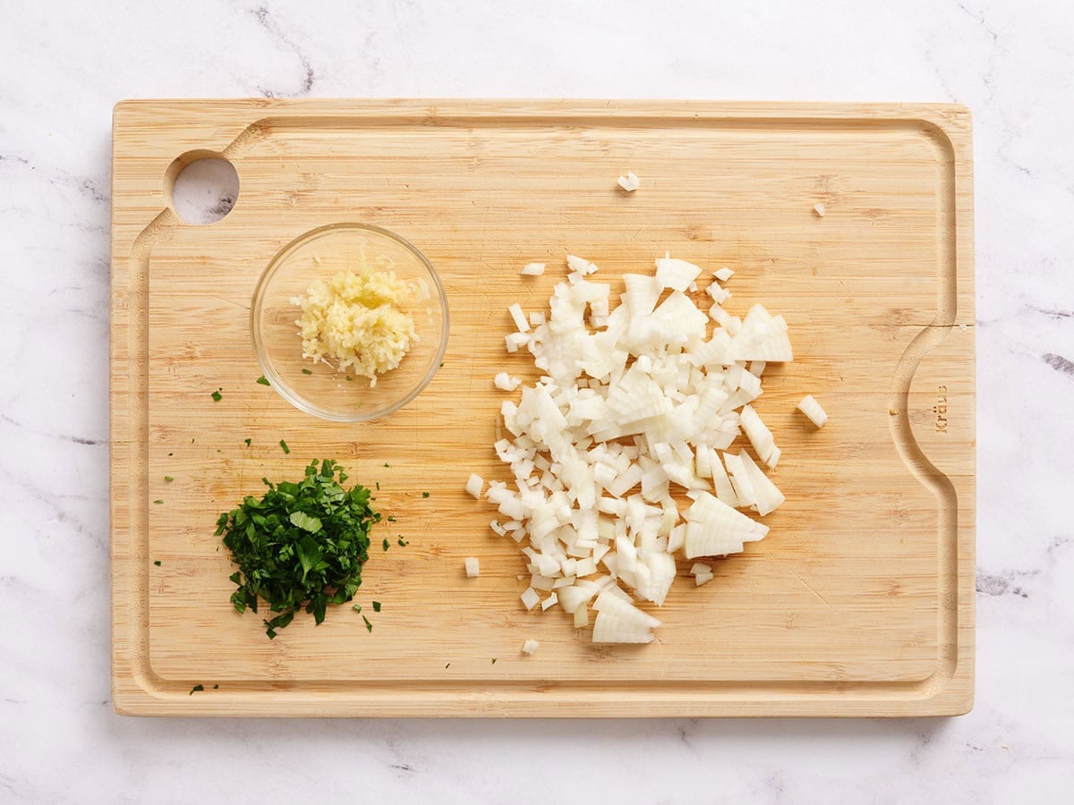 Minced garlic, minced parsley and diced onions on a wooden cutting board.