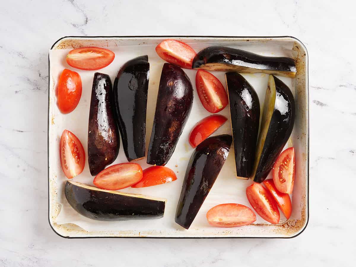 Eggplant and tomato quaters roasting on a baking tray.
