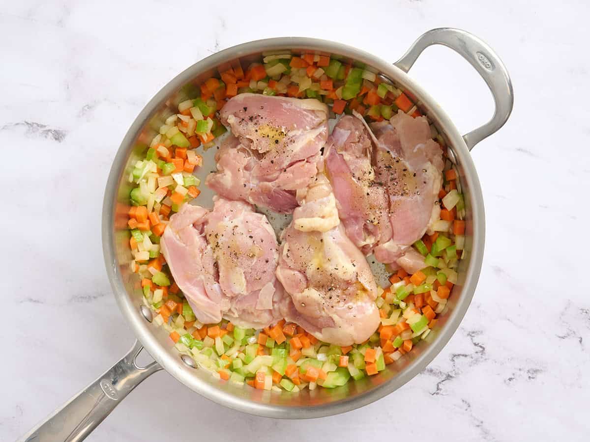 Chicken thighs added to a skillet with sauteed carrots, onions and celery.