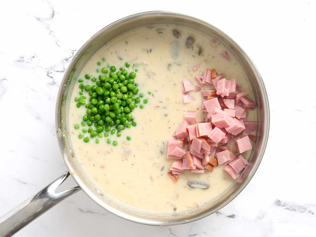 Peas and diced ham added to a skillet of creamy sauce.
