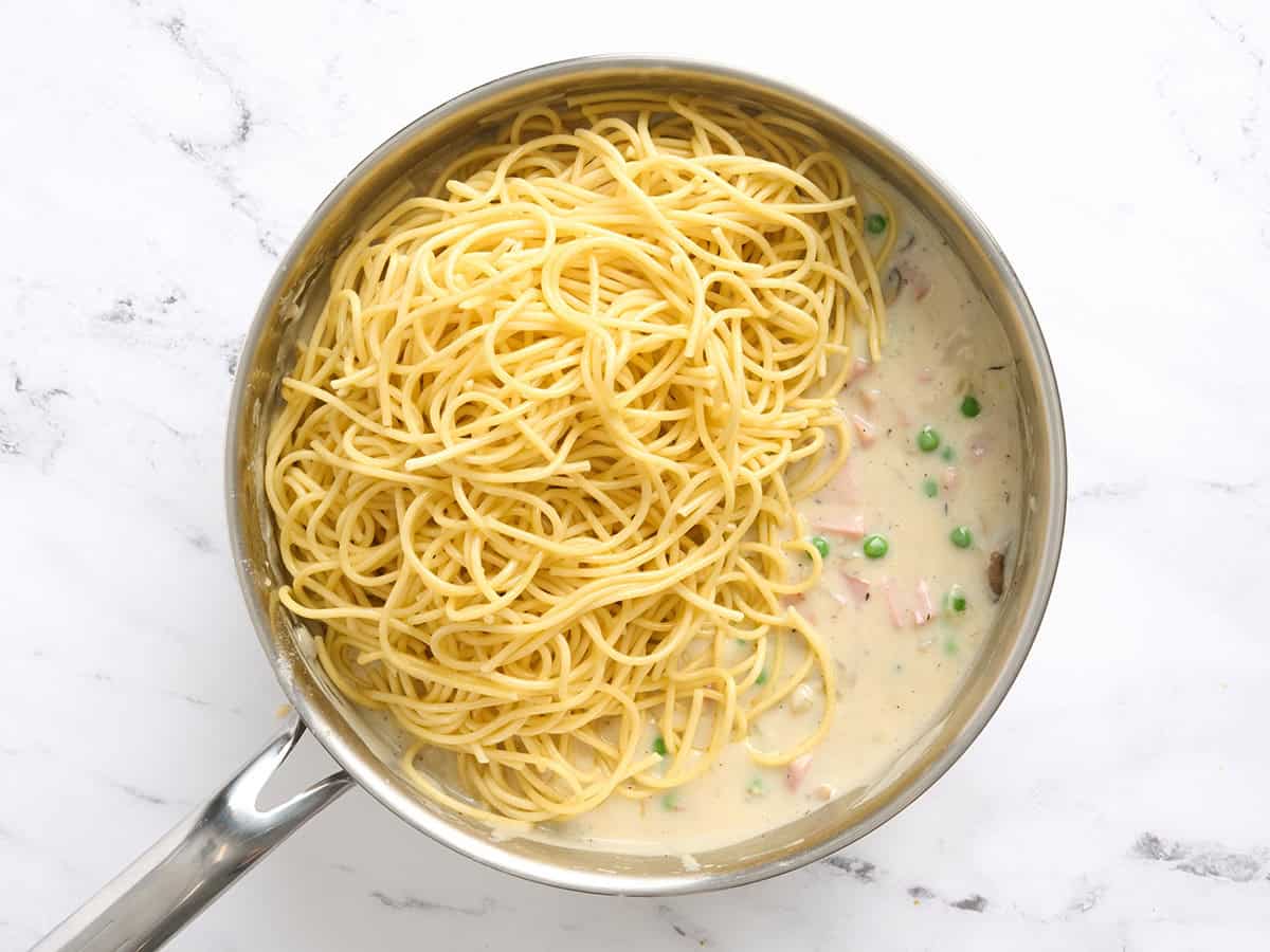 Spaghetti added to a skillet of creamy ham tetrazzini sauce.
