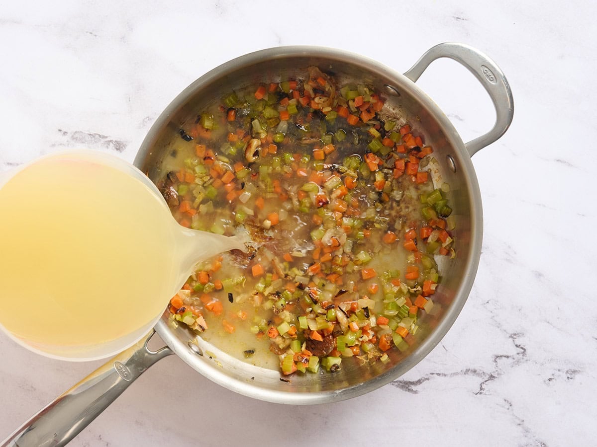 Broth being poured into softened carrots, onions and celery for chicken broth bowls.