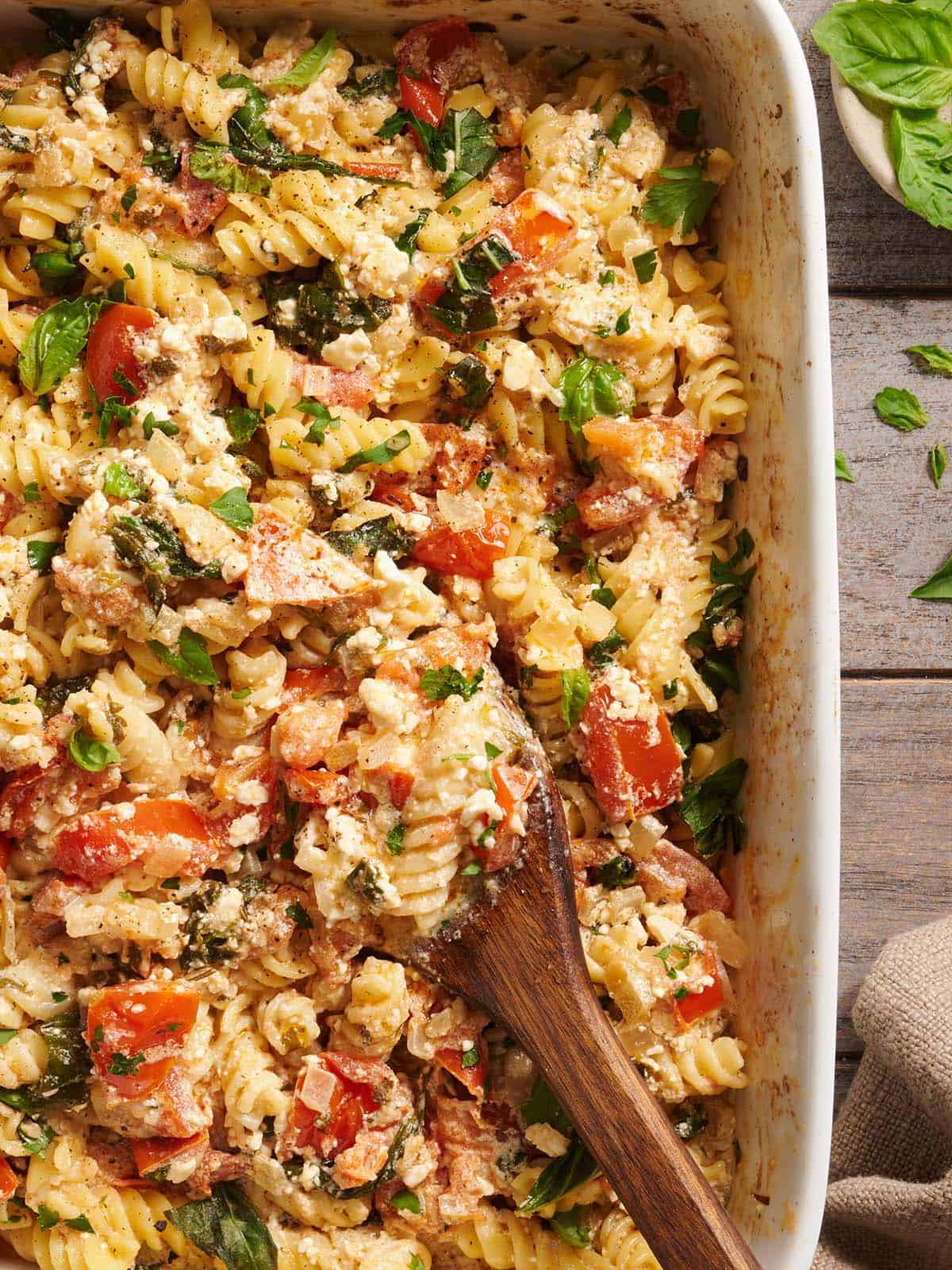 Overhead close up view of baked feta pasta in a baking dish with a wooden spoon.