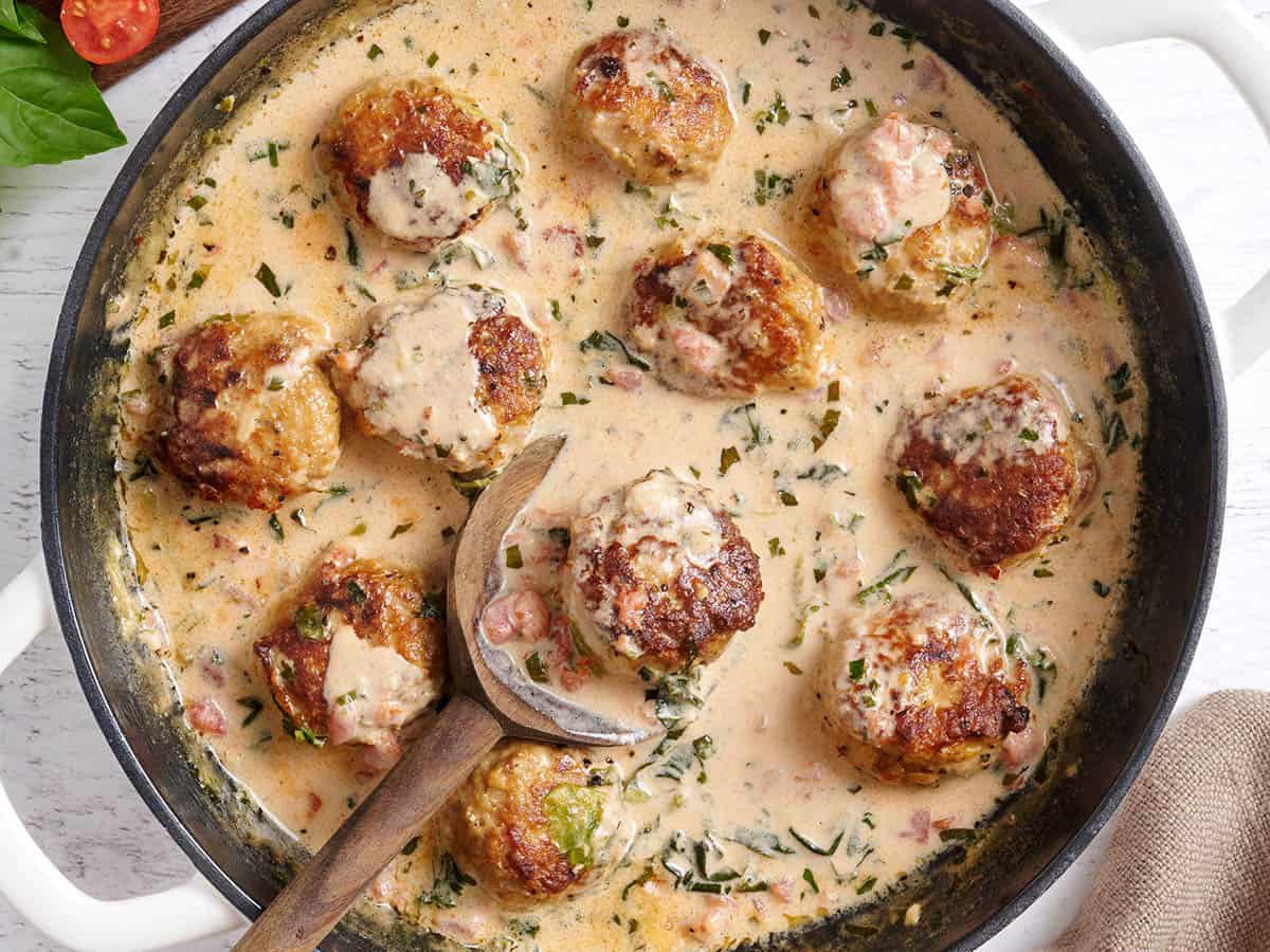 Overhead view of marry meatballs in a skillet with a wooden spoon.