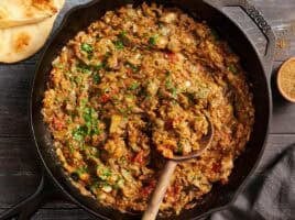 Overhead view of eggplant curry in a skillet with a wooden spoon.