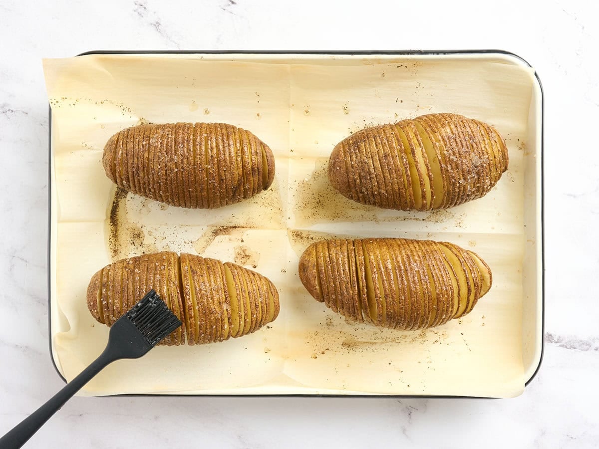 Hasselback potatoes being brushed with seasoned oil part way through baking.
