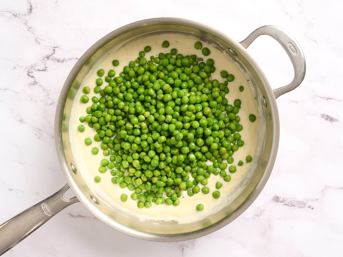 Peas added to a cream sauce in a skillet.