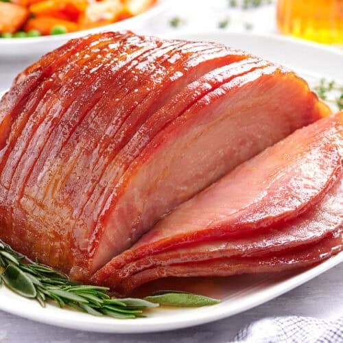 Side view of sliced honey glazed ham on a plate with herbs.
