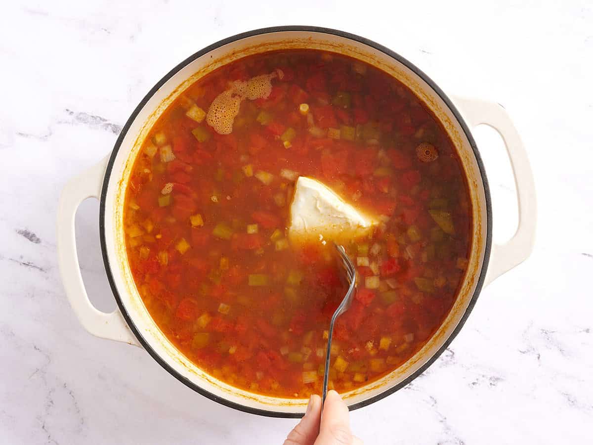 A fork adding cream cheese to a pot of chicken taco soup.