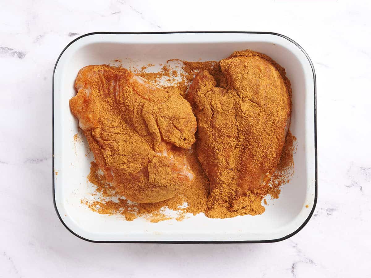 Two chicken breasts covered in taco seasoning in a baking dish.