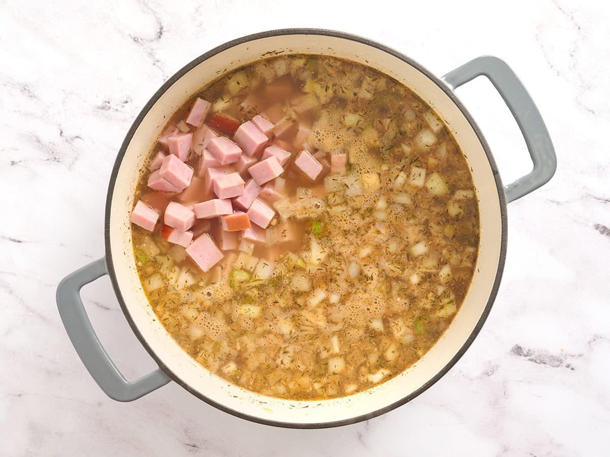 Diced ham added to a pot of broth and vegetables.