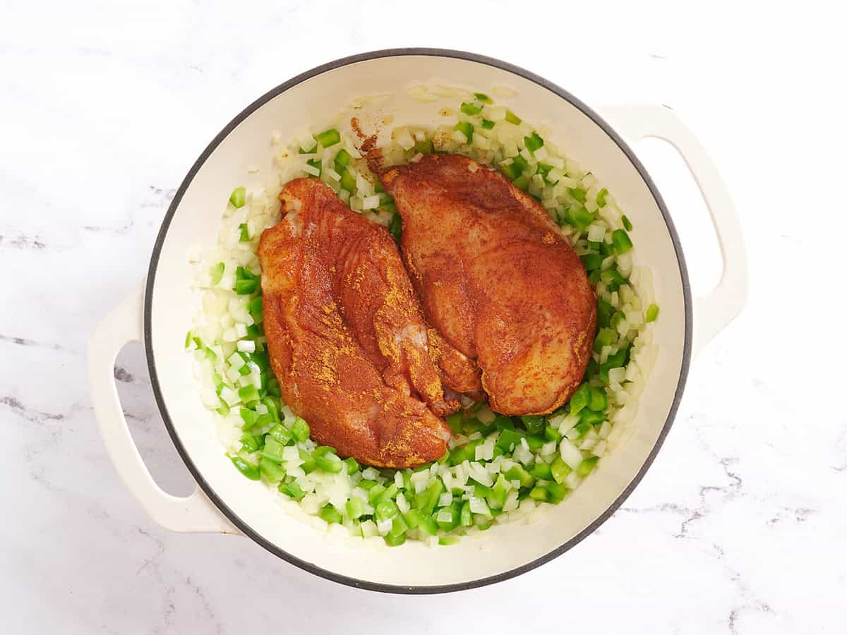 Seasoned chicken breasts added to a pot with sliced green bell pepper and onions.