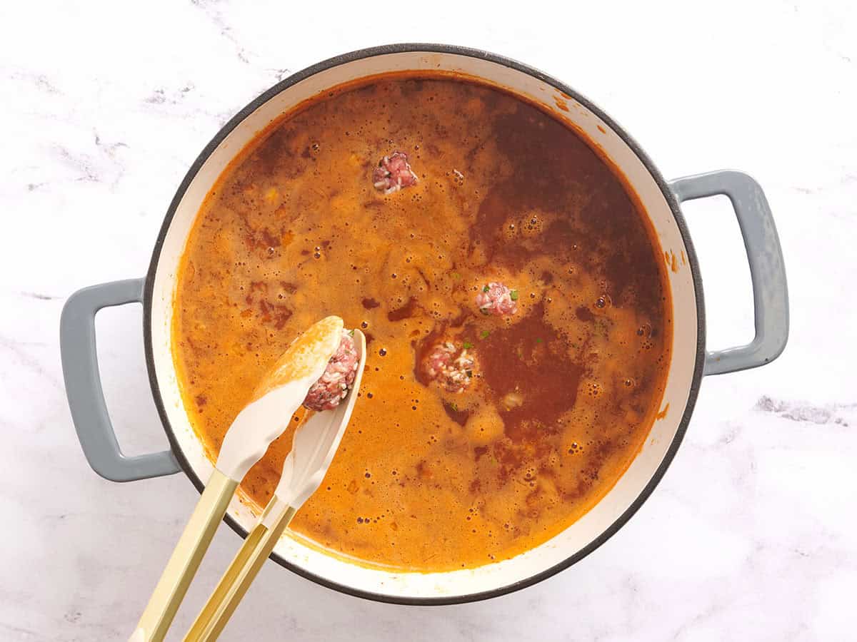 Meatballs being added to a pot of Albóndigas.