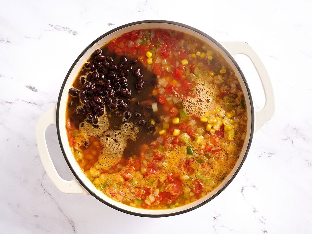 Corn and canned beans added to a pot of chicken taco soup.