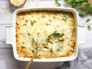 Overhead view of a casserole dish of baked pasta with spring veggies and a spoon.