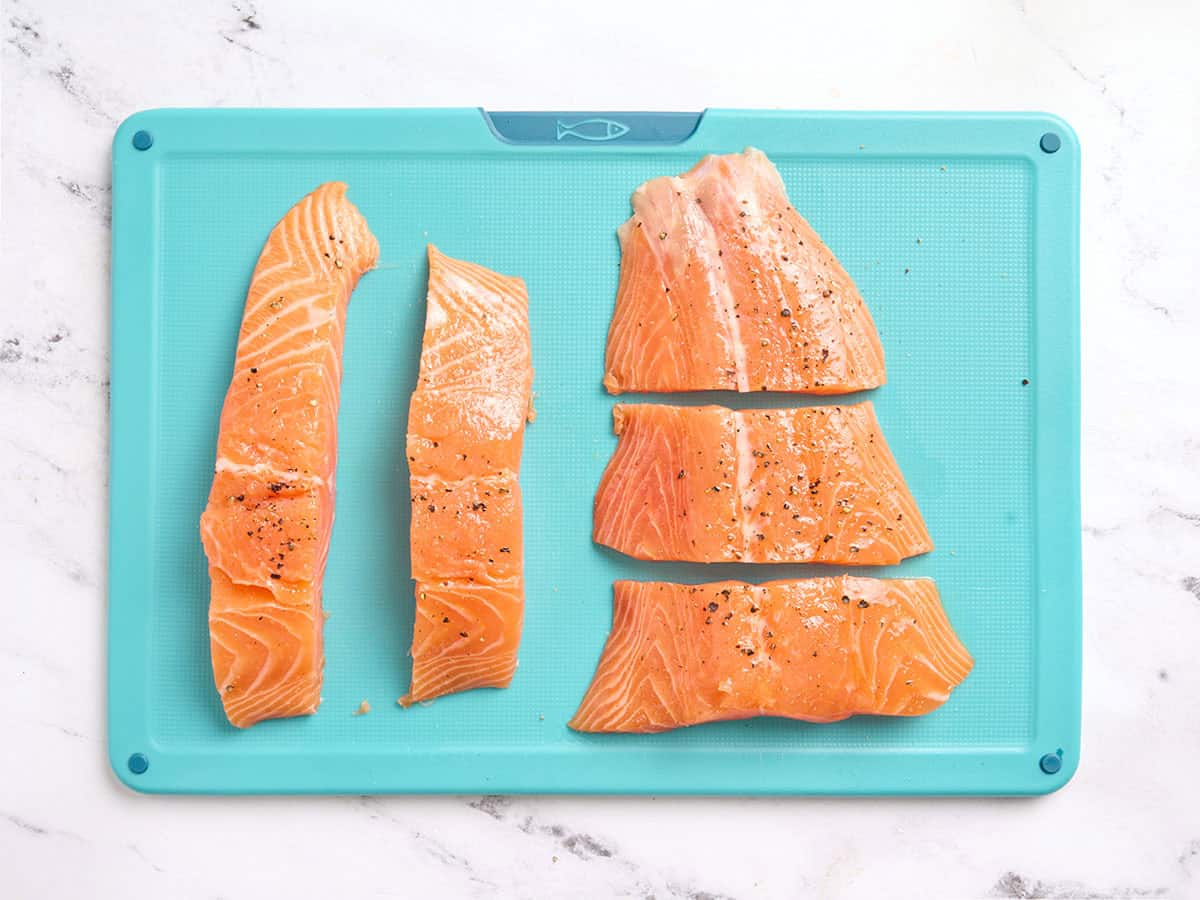 A salmon fillet sliced into 5 pieces and covered with oil and seasonings.