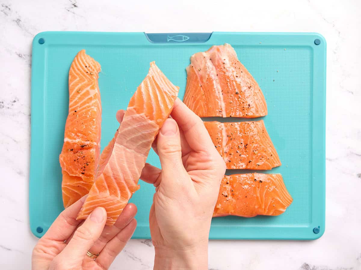 Hands holding a piece of salmon showing what it looks like with the skin removed.
