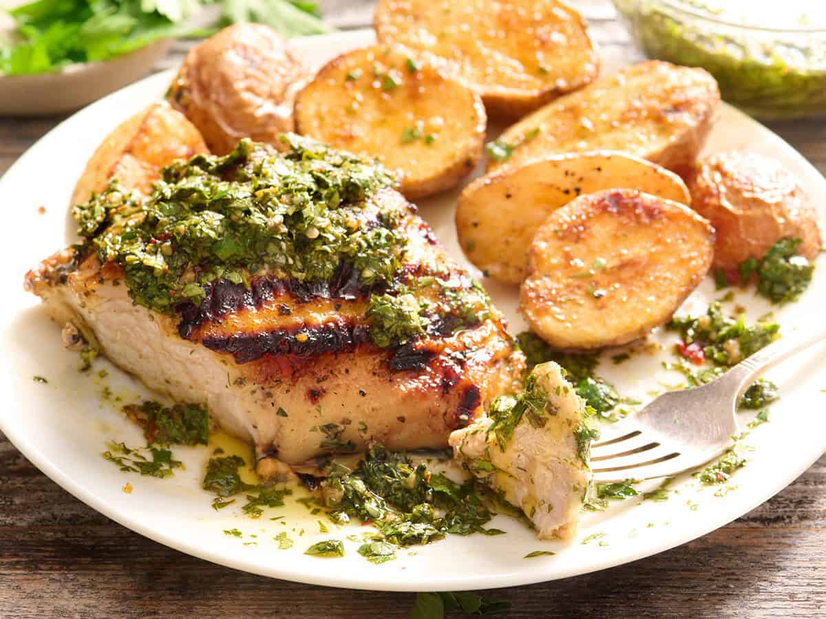 Side view of chimichurri grilled chicken on a plate with roasted potatoes.