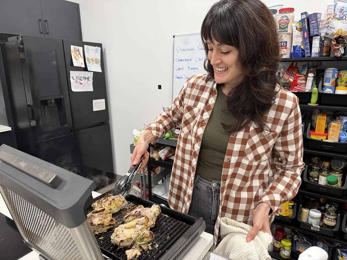 A women cooking chimichurri grilled chicken on a grill in the Budget Bytes studio.