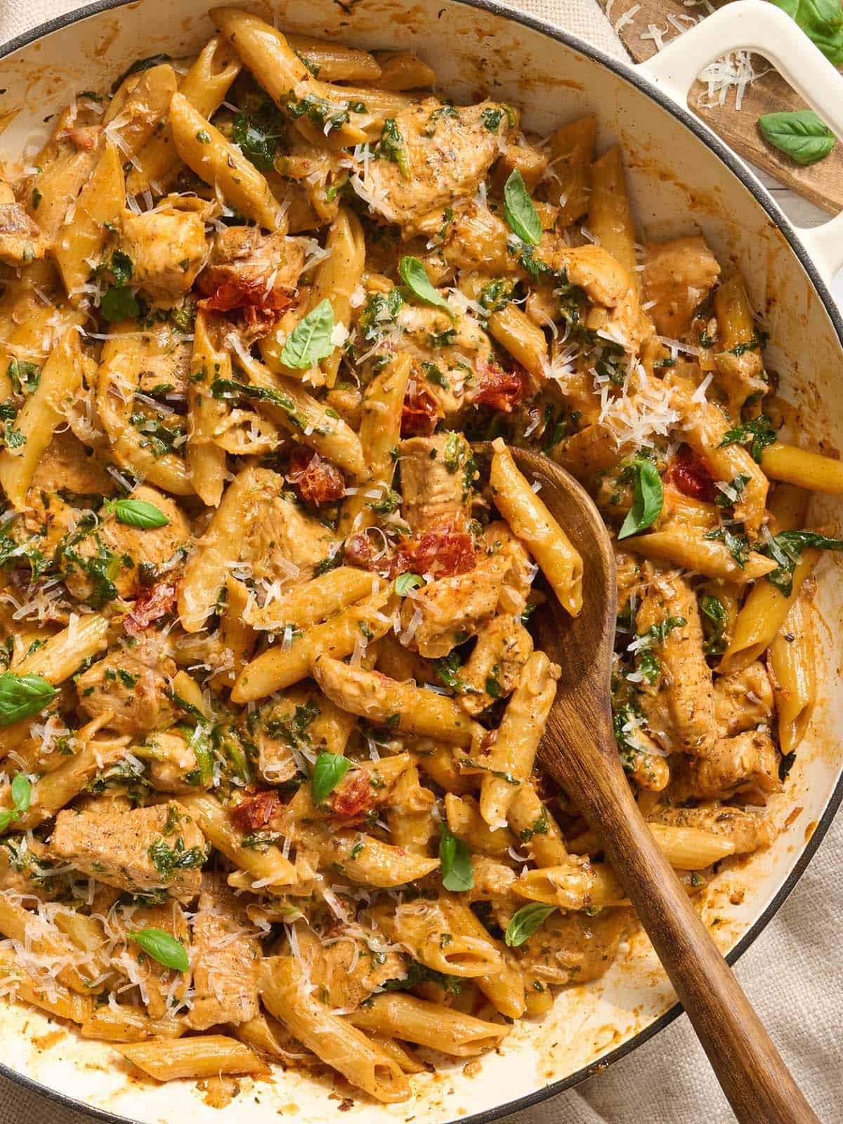 Overhead of marry me chicken pasta in a pot with a wooden spoon.