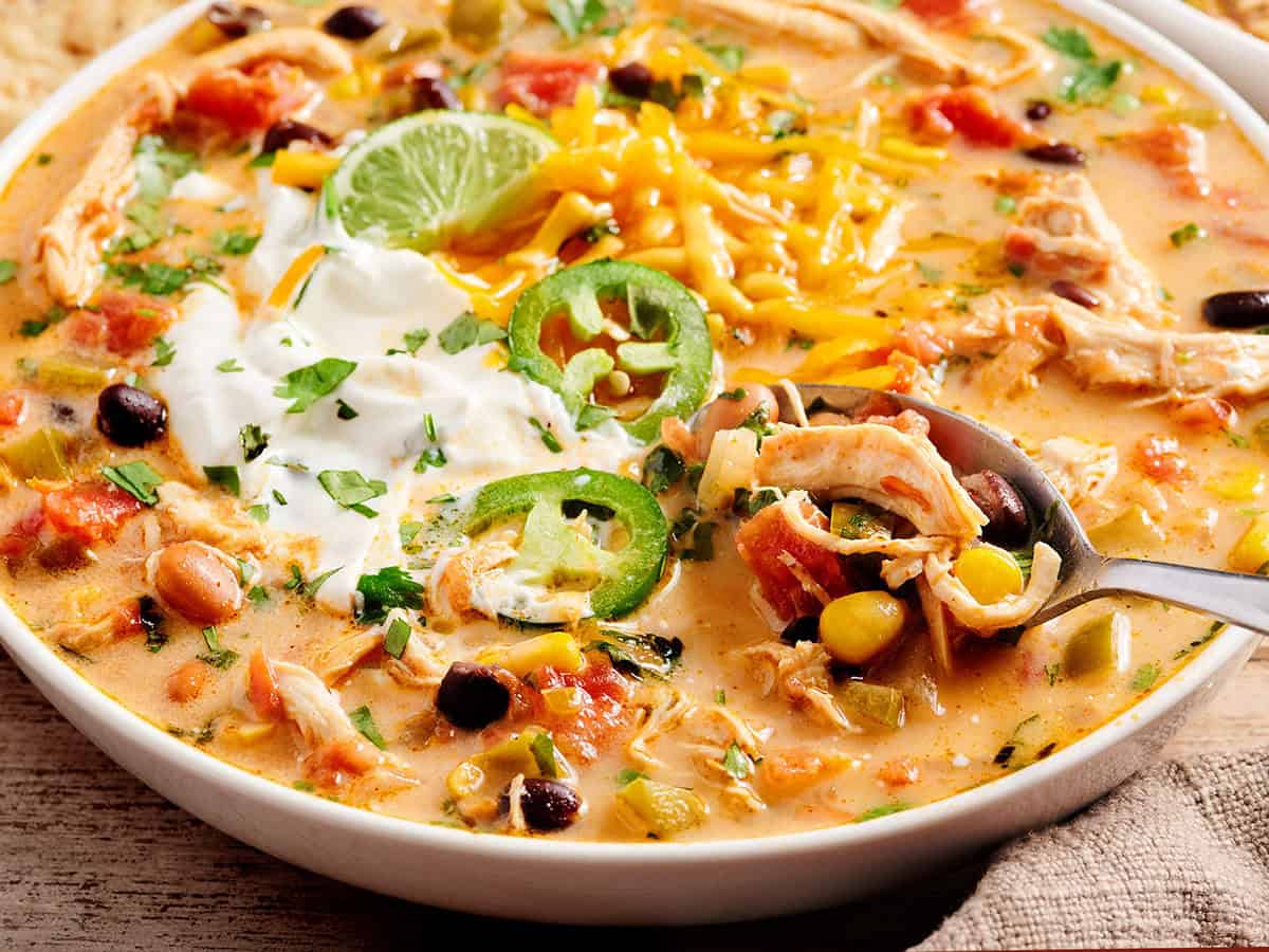 Side close up of chicken taco soup in a bowl with a spoon topped with jalapeno slices and sour cream.
