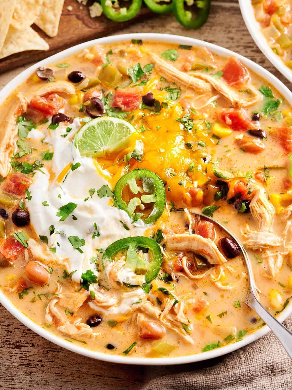 Overhead close up of chicken taco soup in a bowl with a spoon topped with jalapeno slices and sour cream.