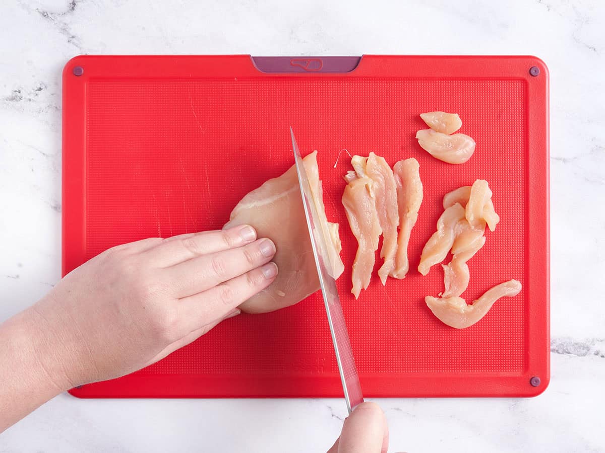 Hands slicing chicken breast on a cutting board.