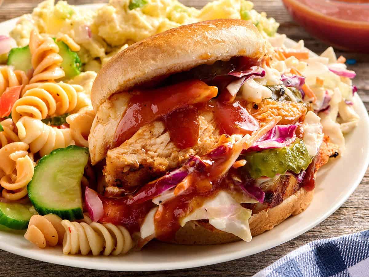 Side view of grilled chicken sandwiches on a plate with pasta salad.