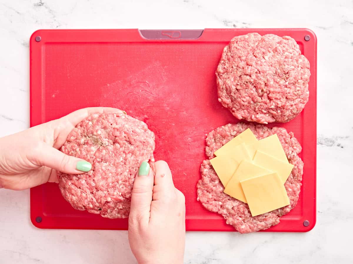 Hands filling burger patties with cheese.
