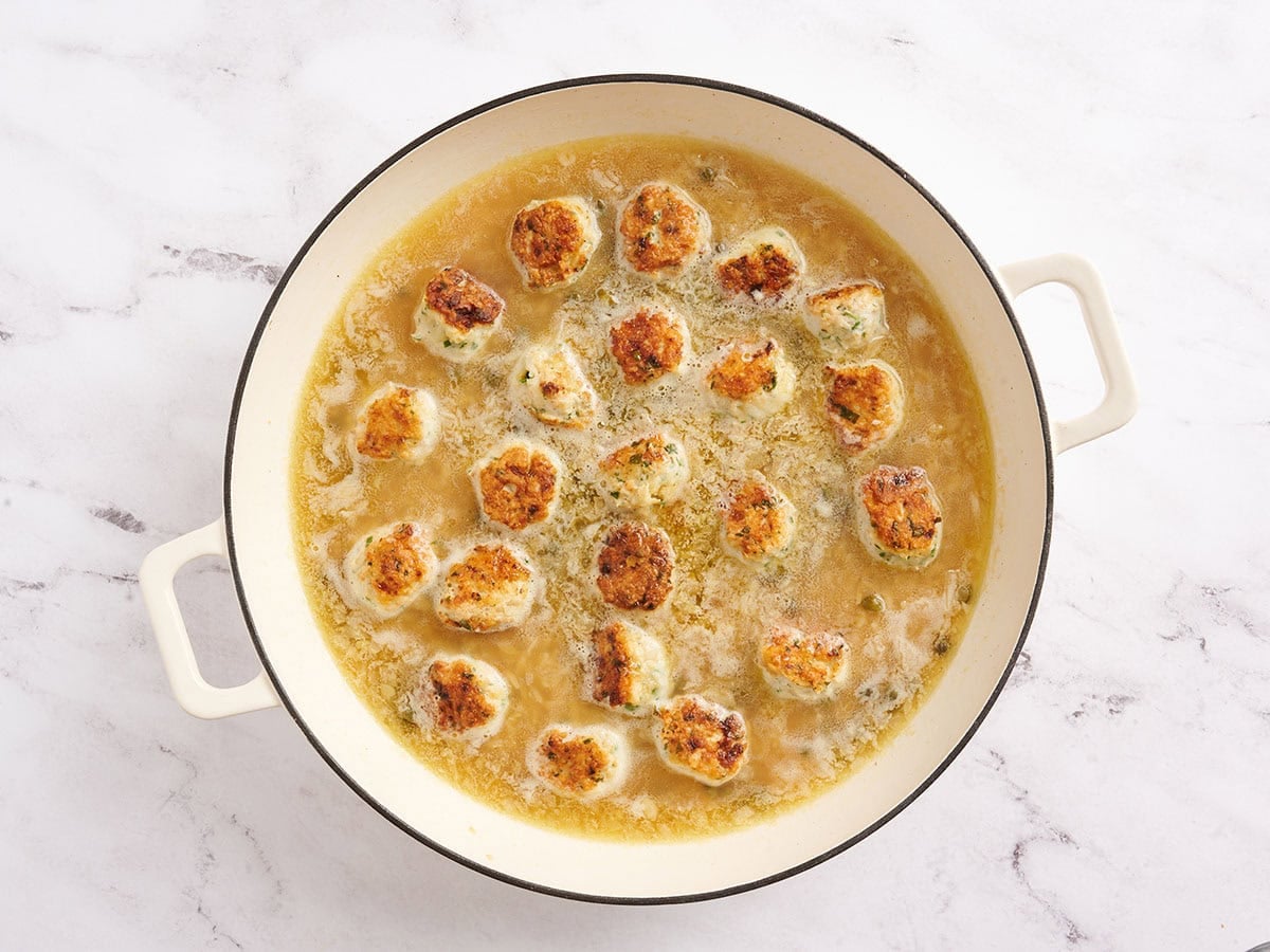 Chicken piccata meatballs added to a skillet with orzo and broth.