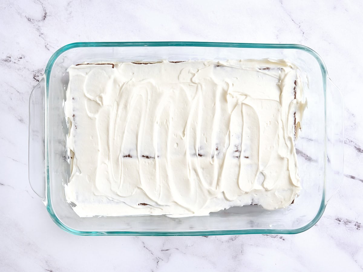 Whipped cream topping added to a baking dish over graham crackers.