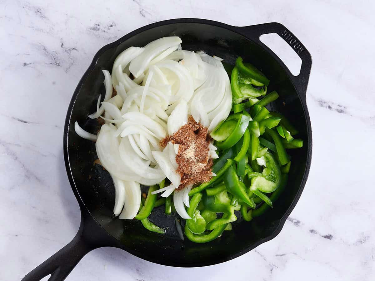 Sliced onion, green peppers and seasoning added to a skillet.
