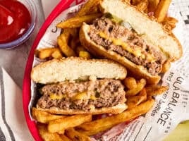 Overhead view of a cheese stuffed juicy lucy burger in a basket with fries.