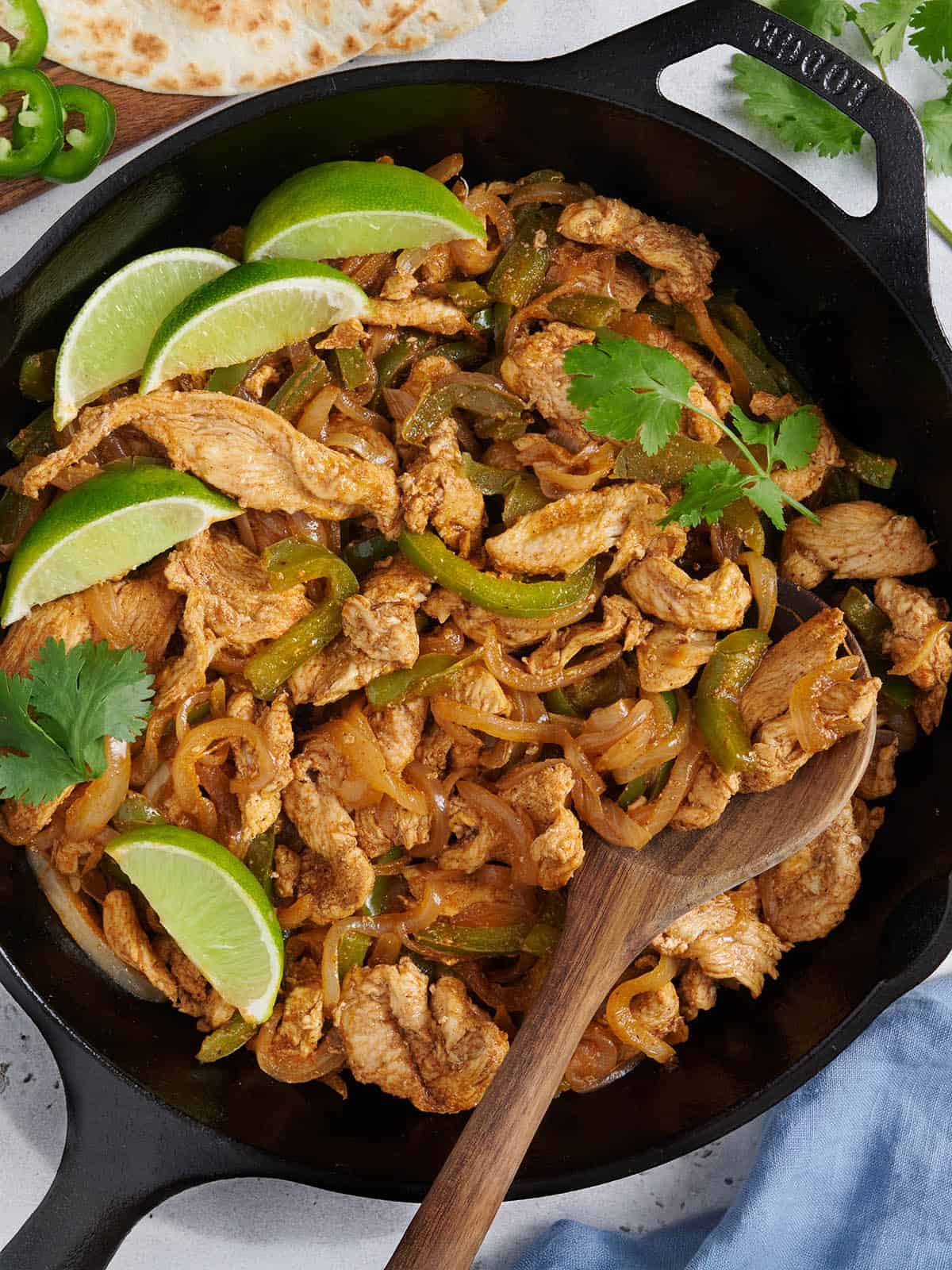 Overhead view of stovetop chicken fajita filling in a skillet with a wooden spoon.