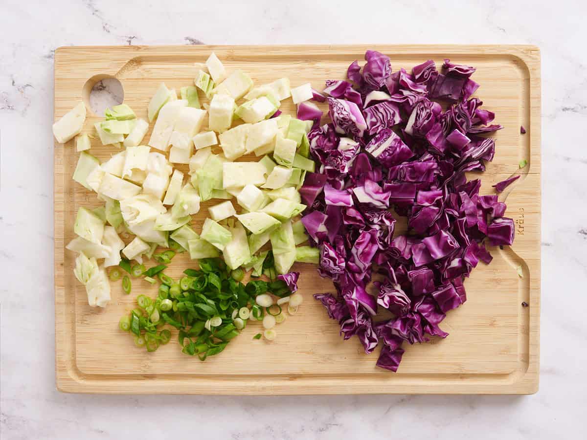 Green and red cabbage chopped on a wooden cutting board.