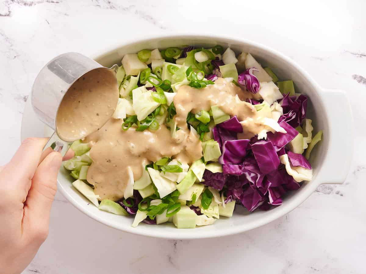 Caesar dressing being added to cabbage slaw in a dish.