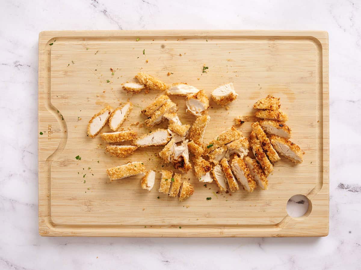 Crispy chicken tenders sliced on a wooden cutting board.